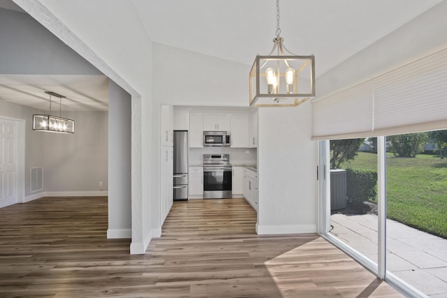 kitchen featuring baseboards, stainless steel appliances, an inviting chandelier, wood finished floors, and white cabinetry