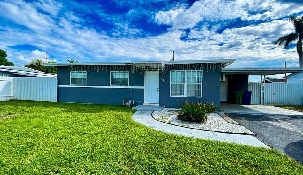 ranch-style home with an attached carport, a front lawn, fence, stucco siding, and driveway