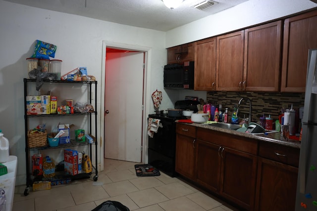 kitchen featuring visible vents, a sink, backsplash, freestanding refrigerator, and black / electric stove