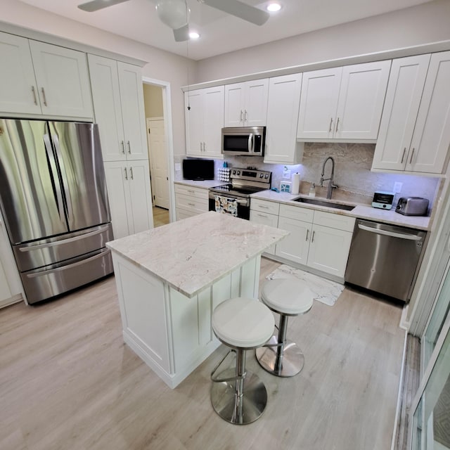 kitchen featuring ceiling fan, decorative backsplash, light wood-style floors, stainless steel appliances, and a sink