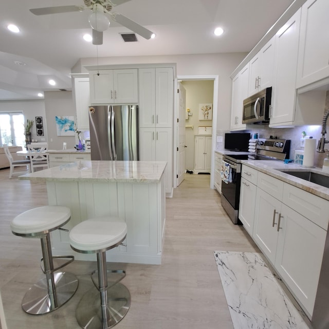 kitchen featuring visible vents, light wood finished floors, white cabinets, appliances with stainless steel finishes, and a center island