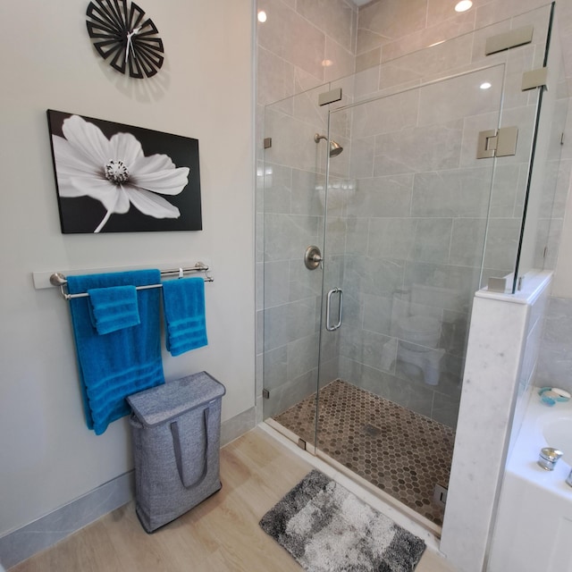 bathroom featuring a bath, a shower stall, baseboards, and wood finished floors