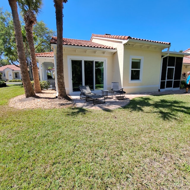 rear view of house featuring a patio, a tile roof, a lawn, and stucco siding