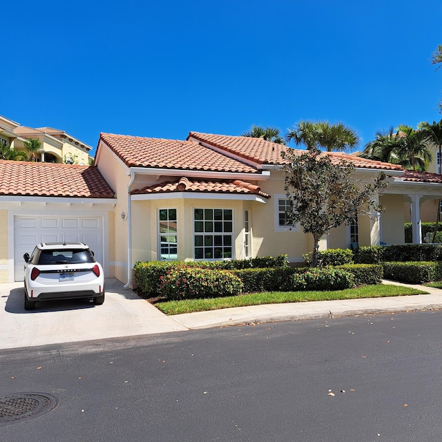 mediterranean / spanish-style house featuring a tile roof, stucco siding, concrete driveway, and a garage