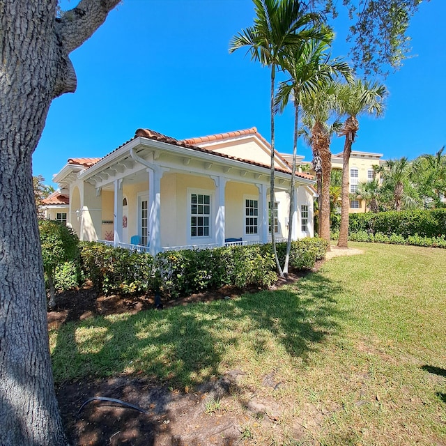 view of side of property featuring stucco siding, a lawn, covered porch, and a tile roof