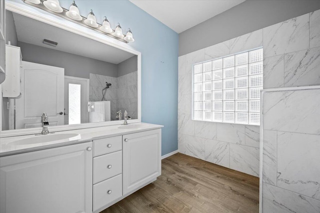 bathroom with a sink, tiled shower, wood finished floors, and double vanity