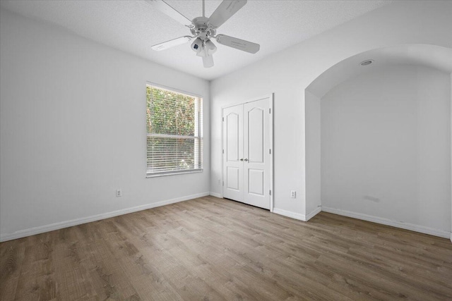 unfurnished bedroom featuring ceiling fan, baseboards, a closet, wood finished floors, and arched walkways