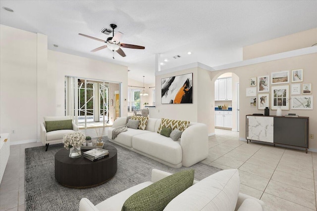 living room featuring a ceiling fan, light tile patterned flooring, visible vents, and arched walkways