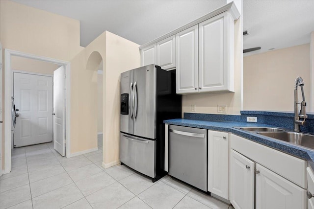 kitchen with a sink, dark countertops, white cabinetry, appliances with stainless steel finishes, and light tile patterned floors