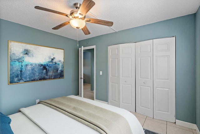 bedroom with a ceiling fan, baseboards, light tile patterned flooring, a closet, and a textured ceiling