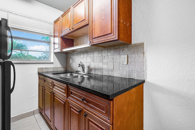 kitchen with a sink, tasteful backsplash, freestanding refrigerator, light tile patterned floors, and baseboards