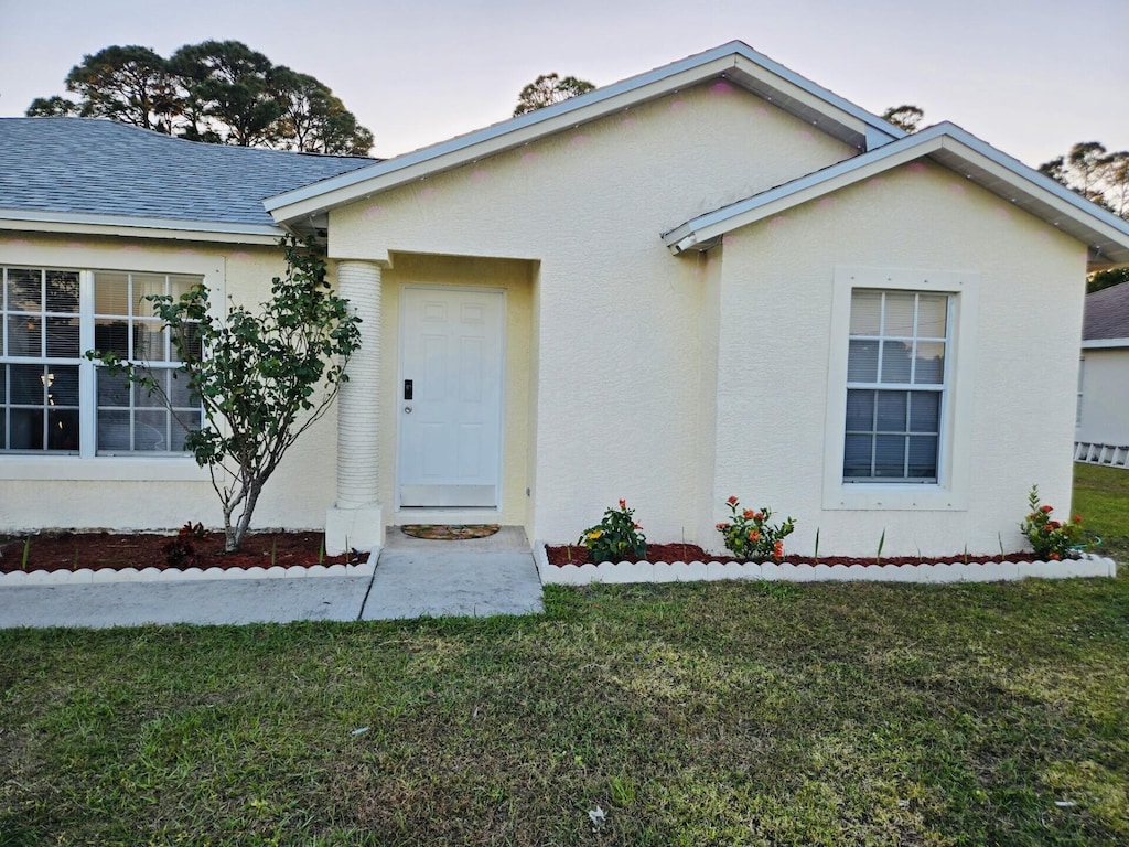 view of front of house featuring a front yard, roof with shingles, and stucco siding