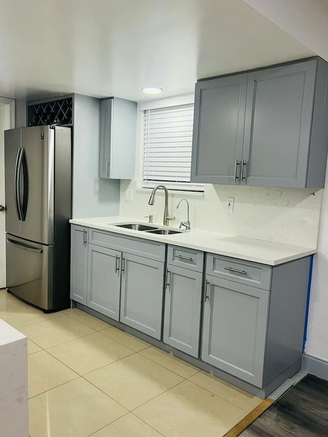 kitchen with gray cabinets, a sink, freestanding refrigerator, light countertops, and light tile patterned floors