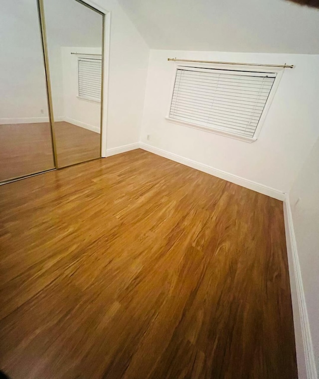 unfurnished bedroom featuring a closet, vaulted ceiling, baseboards, and wood finished floors