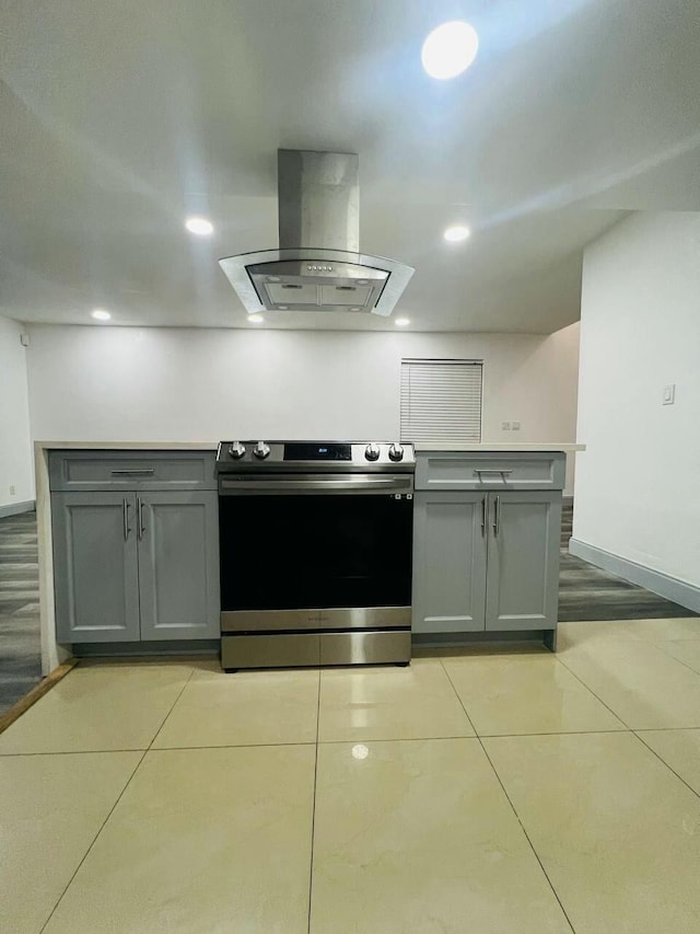 kitchen with light tile patterned floors, island exhaust hood, gray cabinets, and stainless steel range with electric cooktop