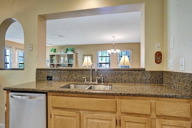 kitchen with light brown cabinetry, dishwasher, dark stone countertops, arched walkways, and a sink