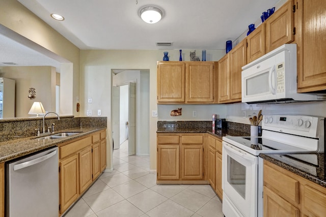 kitchen featuring visible vents, dark stone counters, light tile patterned floors, white appliances, and a sink