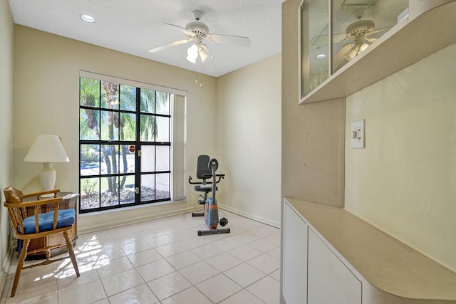 workout area with light tile patterned floors, a ceiling fan, baseboards, and a textured ceiling