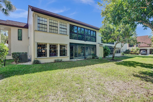 rear view of house with stucco siding, a lawn, and central AC