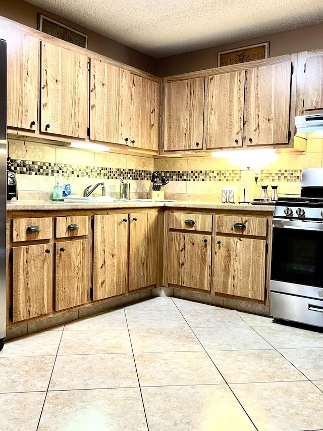 kitchen featuring under cabinet range hood, light countertops, light tile patterned floors, decorative backsplash, and gas range