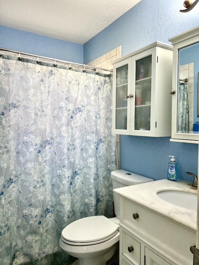 full bath featuring toilet, a shower with shower curtain, vanity, a textured wall, and a textured ceiling