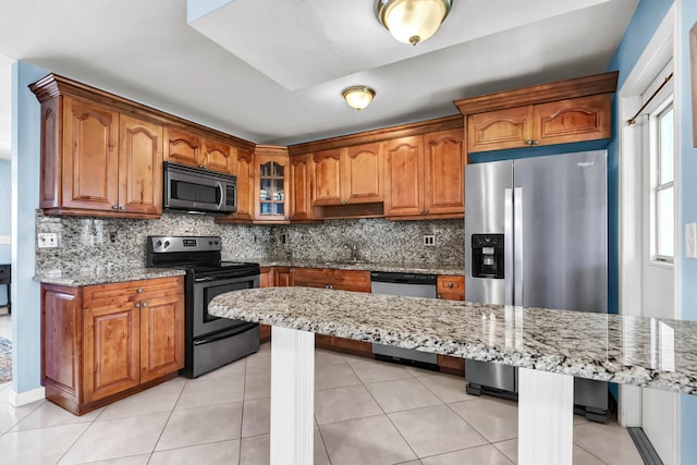 kitchen featuring a kitchen bar, brown cabinetry, light stone countertops, and appliances with stainless steel finishes