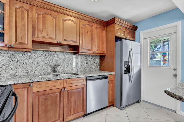 kitchen featuring glass insert cabinets, light stone counters, brown cabinets, stainless steel appliances, and a sink