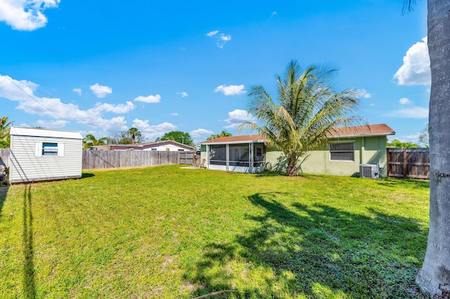 view of yard with a fenced backyard, a sunroom, central AC, an outdoor structure, and a storage unit