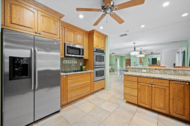 kitchen featuring a ceiling fan, light stone counters, stainless steel appliances, light tile patterned flooring, and decorative backsplash