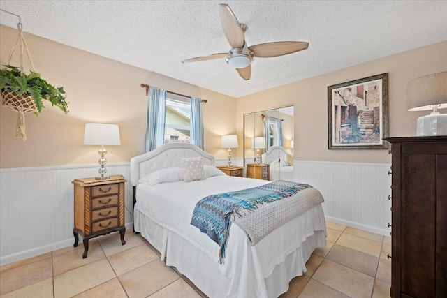 bedroom with a ceiling fan, a textured ceiling, and wainscoting