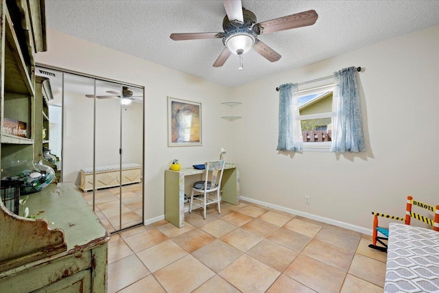 home office featuring light tile patterned floors, a ceiling fan, baseboards, and a textured ceiling