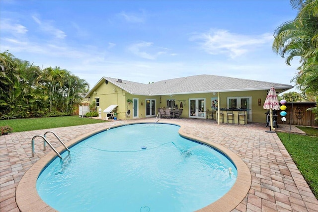 view of pool featuring a patio, a fenced in pool, french doors, a lawn, and outdoor dry bar