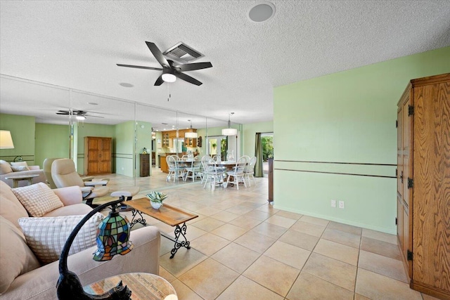 living room featuring visible vents, baseboards, ceiling fan, light tile patterned floors, and a textured ceiling