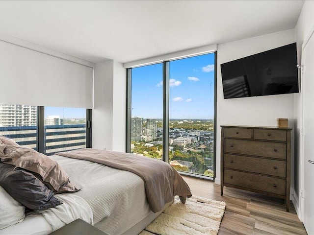 bedroom featuring floor to ceiling windows, a view of city, and wood finished floors