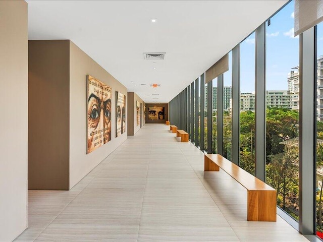 hall featuring light tile patterned flooring, visible vents, floor to ceiling windows, and a city view