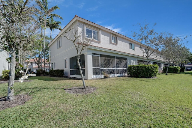 back of property featuring a lawn, a sunroom, and stucco siding