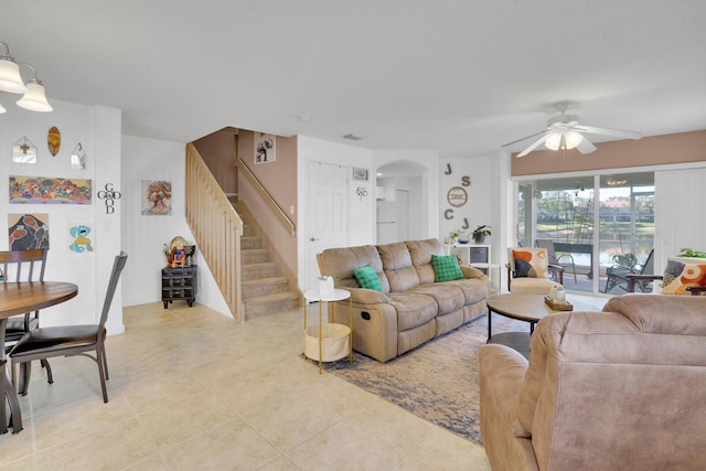 living area featuring stairs, arched walkways, light tile patterned flooring, and a ceiling fan