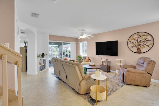 living room featuring visible vents, baseboards, light tile patterned floors, arched walkways, and a ceiling fan