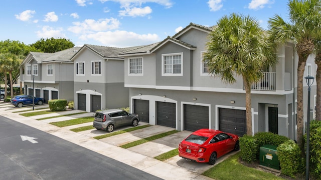 view of property featuring a tile roof, a garage, driveway, and stucco siding