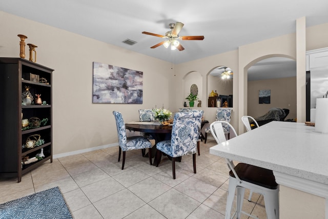 dining space featuring light tile patterned floors, a ceiling fan, visible vents, baseboards, and arched walkways