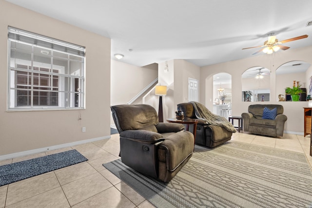 living room with tile patterned flooring, baseboards, ceiling fan, stairs, and arched walkways