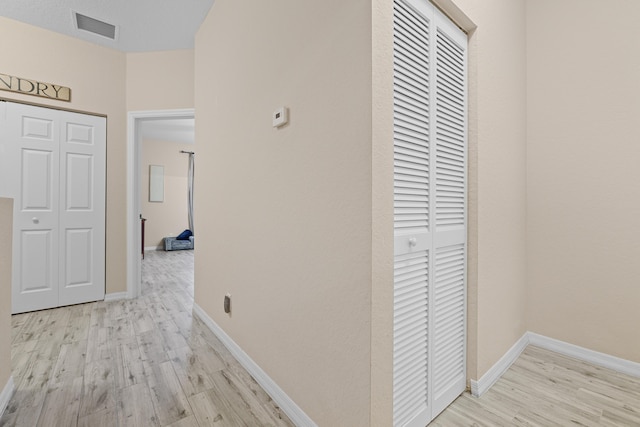 hall with visible vents, baseboards, and wood finished floors