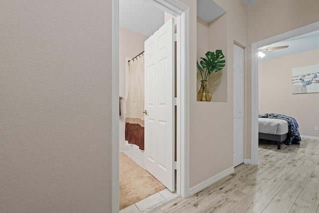 hallway with light wood-type flooring, baseboards, and a textured wall