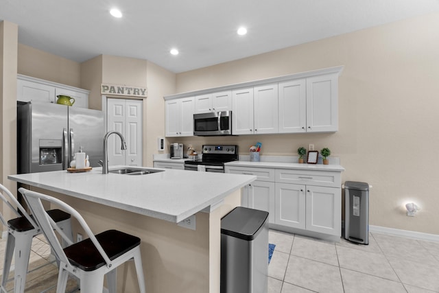 kitchen with white cabinetry, an island with sink, a sink, appliances with stainless steel finishes, and a kitchen bar