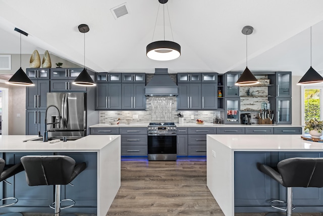 kitchen with stainless steel appliances, custom exhaust hood, an island with sink, and vaulted ceiling