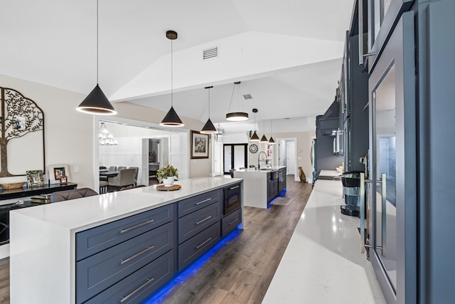 kitchen with visible vents, stainless steel refrigerator, a spacious island, wood finished floors, and lofted ceiling