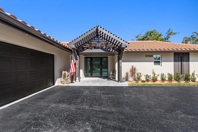 view of front of property with driveway, an attached garage, a pergola, stucco siding, and a tiled roof