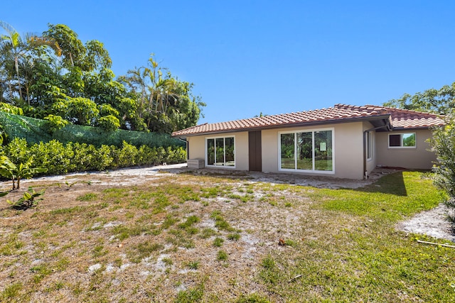 rear view of property with stucco siding, a tiled roof, and a yard