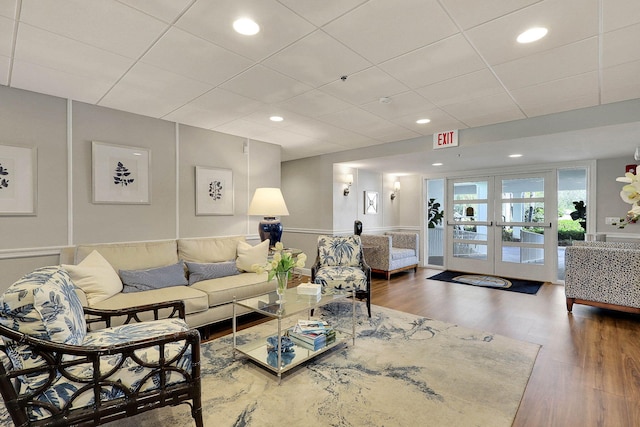 living room with a drop ceiling, recessed lighting, french doors, and wood finished floors