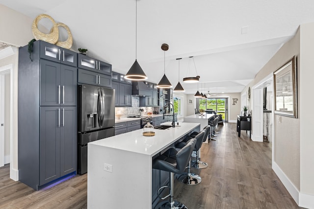 kitchen featuring a kitchen bar, a kitchen island with sink, backsplash, stainless steel fridge with ice dispenser, and light countertops